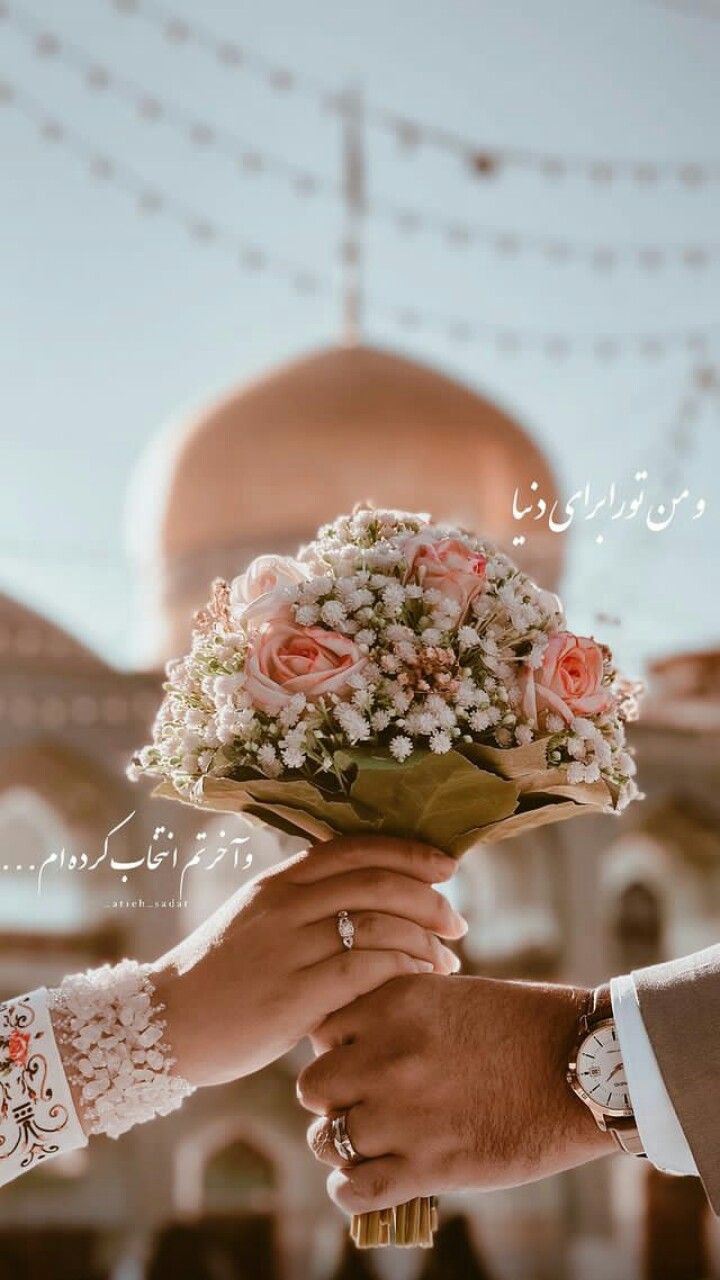 دست عروس و داماد دسته گل رز هلویی را مقابل گنبد طلایی و ریسه نور نگه داشته‌اند
