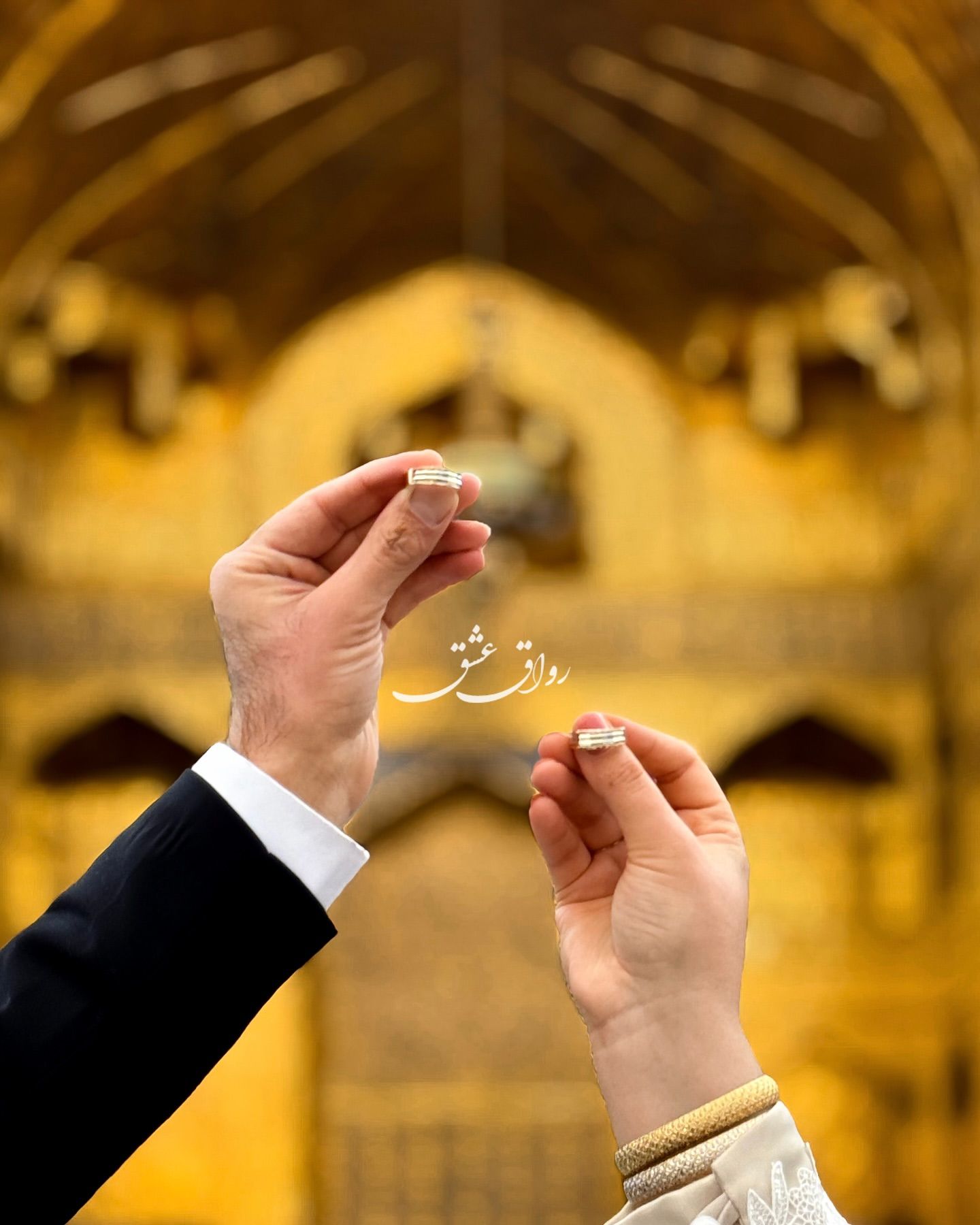 دست عروس و داماد هر کدام یک حلقه را مقابل رواق طلاکاری‌شده حرم نگه داشته‌اند